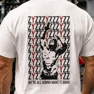 Pode incluir: Uma t-shirt branca de manga curta com um gráfico preto e vermelho nas costas. O design inclui o texto repetido ZYZZYZZYZZ e a silhueta de um fisiculturista a posar, com o texto WE'RE ALL GONNA MAKE IT BRAH na parte inferior do gráfico.