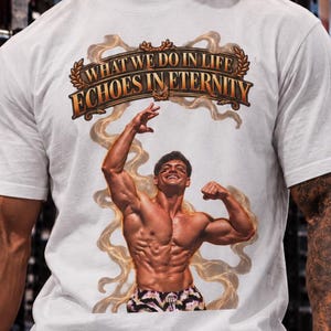 Könnte beinhalten: Ein weißes kurzärmeliges T-Shirt mit einem Grafikdruck einer muskulösen Person, die mit erhobenen Armen posiert. Über der Figur steht der Text "WHAT WE DO IN LIFE ECHOES IN ETERNITY" in einer stilisierten Schrift, umgeben von wirbelnden rauchartigen Akzenten.
