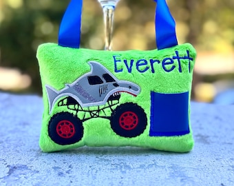 Könnte beinhalten: Eine hellgrüne Plüschtasche mit blauen Griffen und einer blauen Tasche. Die Tasche zeigt ein Hai-Monster-Truck-Design mit dem Namen "Everett" in Blau gestickt.