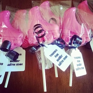 May include: Pink, foot-shaped lollipops in clear cellophane, tied with black ribbon and tags that read "Thanks for rollin' with me!". The lollipops are on white sticks, ready to be enjoyed.