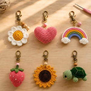 Pode incluir: Um conjunto de seis porta-chaves de croché com uma margarida branca, um coração rosa, um arco-íris com nuvens, um morango vermelho, um girassol amarelo e uma tartaruga verde. Cada item inclui um fecho mosquetão de metal cor de bronze.