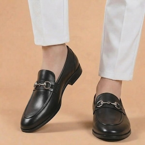 Puede incluir: Mocasines de cuero negro con detalle de adorno de caballo plateado. Estos zapatos clásicos tienen una puntera redondeada y un tacón bajo. Los mocasines se llevan con pantalones blancos.