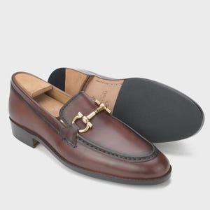 Handmade mahogany brown leather horsebit loafers for men featuring a gold metal horsebit, moc toe stitching, premium leather construction, and classic slip-on design for formal and business casual wear.