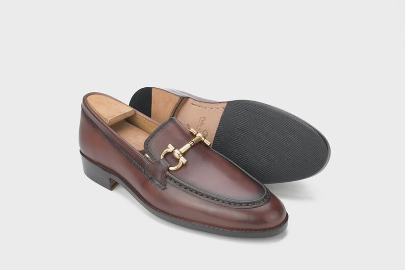 Handmade mahogany brown leather horsebit loafers for men featuring a gold metal horsebit, moc toe stitching, premium leather construction, and classic slip-on design for formal and business casual wear.