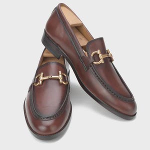 Handmade mahogany brown leather horsebit loafers for men featuring a gold metal horsebit, moc toe stitching, premium leather construction, and classic slip-on design for formal and business casual wear.