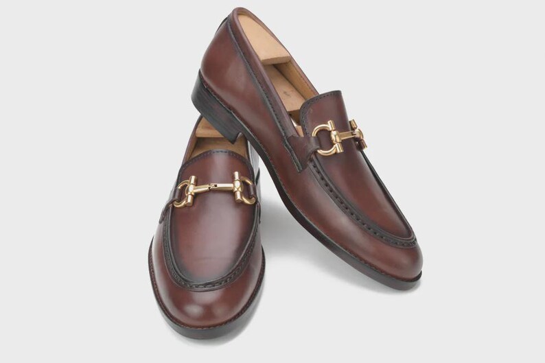 Handmade mahogany brown leather horsebit loafers for men featuring a gold metal horsebit, moc toe stitching, premium leather construction, and classic slip-on design for formal and business casual wear.