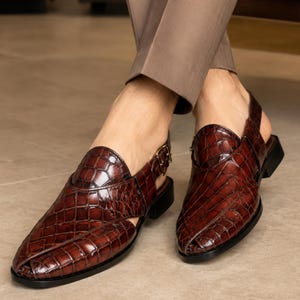 Luxury brown crocodile-textured leather slingback sandals for men with pointed toe and buckle strap detail, handmade premium formal footwear styled with beige trousers in an elegant indoor setting.