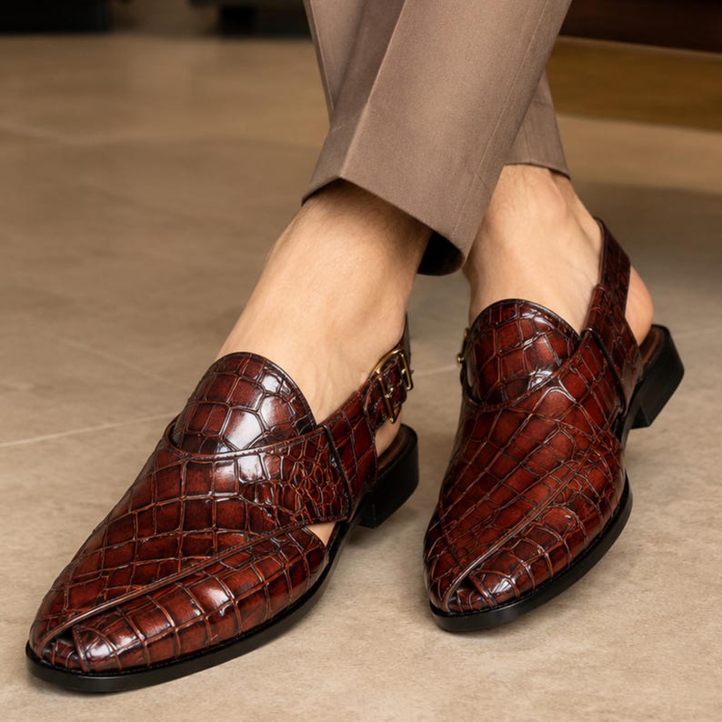 Luxury brown crocodile-textured leather slingback sandals for men with pointed toe and buckle strap detail, handmade premium formal footwear styled with beige trousers in an elegant indoor setting.