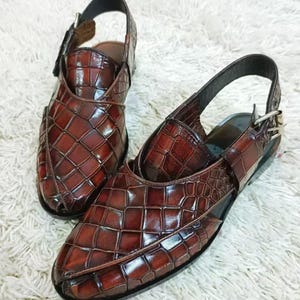 Luxury brown crocodile-textured leather slingback sandals for men with pointed toe and buckle strap detail, handmade premium formal footwear styled with beige trousers in an elegant indoor setting.