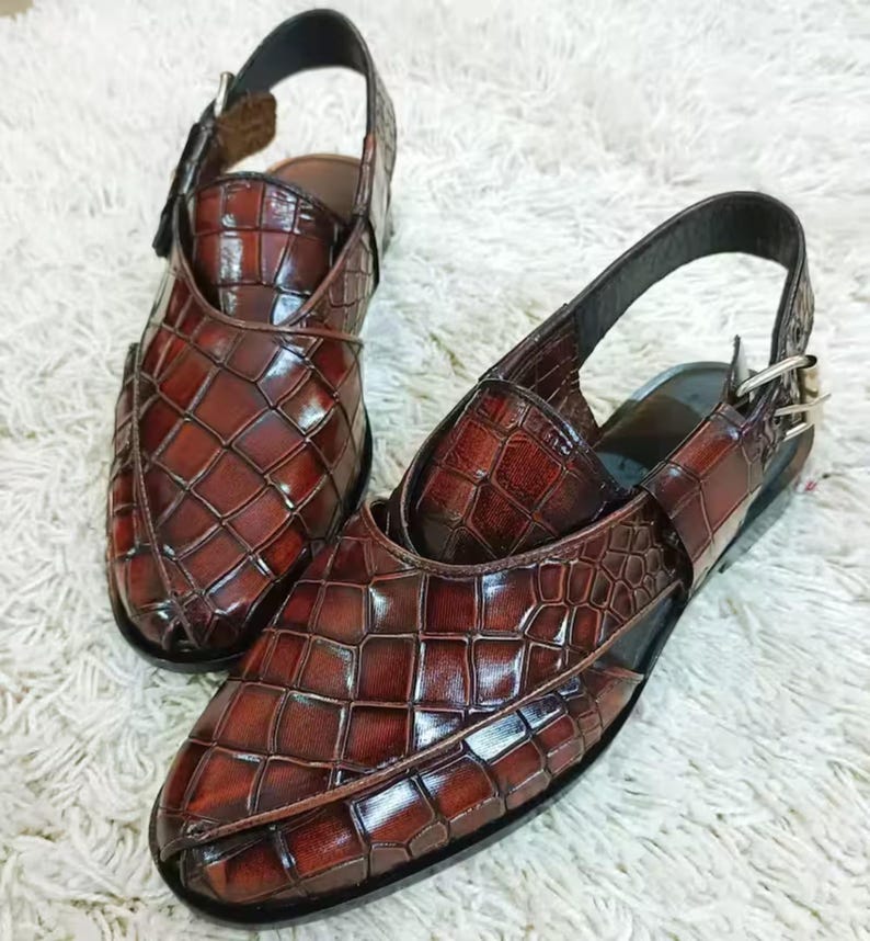 Luxury brown crocodile-textured leather slingback sandals for men with pointed toe and buckle strap detail, handmade premium formal footwear styled with beige trousers in an elegant indoor setting.