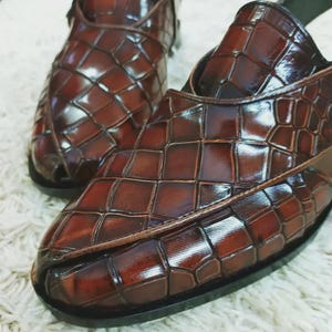 Luxury brown crocodile-textured leather slingback sandals for men with pointed toe and buckle strap detail, handmade premium formal footwear styled with beige trousers in an elegant indoor setting.