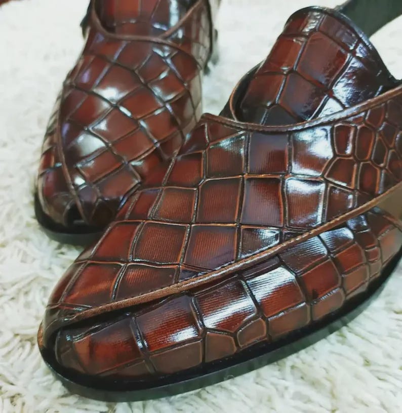 Luxury brown crocodile-textured leather slingback sandals for men with pointed toe and buckle strap detail, handmade premium formal footwear styled with beige trousers in an elegant indoor setting.