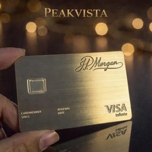 Op de afbeelding: Een goudkleurige Visa Infinite creditcard met het JP Morgan logo. De kaart heeft een geborstelde metalen textuur en de woorden "CARDMEMBER SINCE" en "RENEWAL DATE" zijn zichtbaar. Het woord "PEAKVISTA" staat bovenaan.