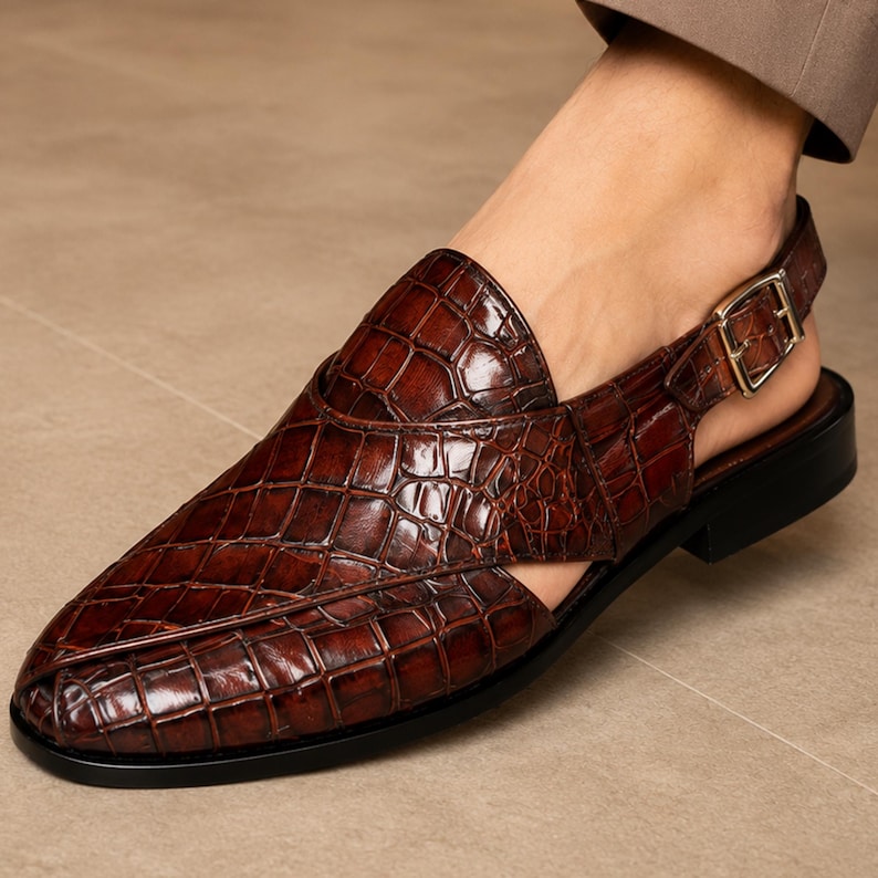 Luxury brown crocodile-textured leather slingback sandals for men with pointed toe and buckle strap detail, handmade premium formal footwear styled with beige trousers in an elegant indoor setting.