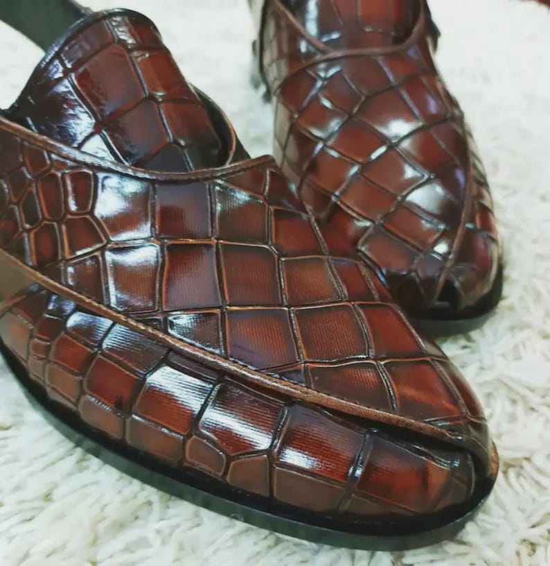 Luxury brown crocodile-textured leather slingback sandals for men with pointed toe and buckle strap detail, handmade premium formal footwear styled with beige trousers in an elegant indoor setting.