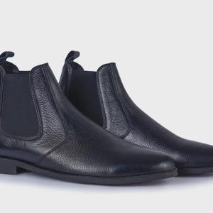 Könnte beinhalten: Ein Paar schwarze Chelsea-Stiefel aus Leder. Die Stiefel haben eine runde Spitze, elastische Seiteneinsätze und eine Zuglasche hinten. Das Leder hat eine strukturierte Oberfläche. Klassischer Stil.