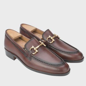 Handmade mahogany brown leather horsebit loafers for men featuring a gold metal horsebit, moc toe stitching, premium leather construction, and classic slip-on design for formal and business casual wear.