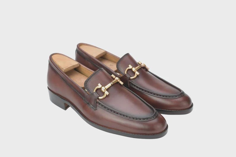 Handmade mahogany brown leather horsebit loafers for men featuring a gold metal horsebit, moc toe stitching, premium leather construction, and classic slip-on design for formal and business casual wear.