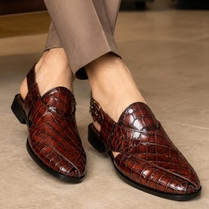 Luxury brown crocodile-textured leather slingback sandals for men with pointed toe and buckle strap detail, handmade premium formal footwear styled with beige trousers in an elegant indoor setting.