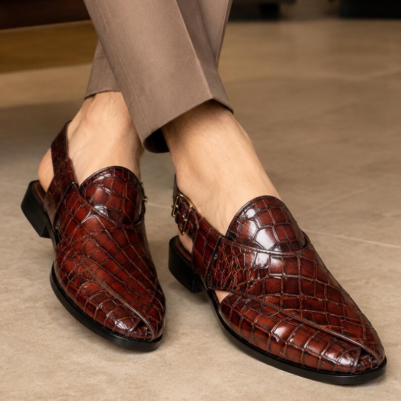 Luxury brown crocodile-textured leather slingback sandals for men with pointed toe and buckle strap detail, handmade premium formal footwear styled with beige trousers in an elegant indoor setting.