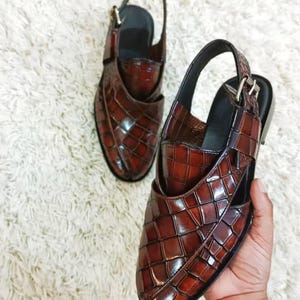 Luxury brown crocodile-textured leather slingback sandals for men with pointed toe and buckle strap detail, handmade premium formal footwear styled with beige trousers in an elegant indoor setting.