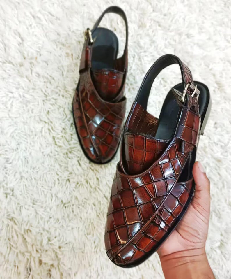 Luxury brown crocodile-textured leather slingback sandals for men with pointed toe and buckle strap detail, handmade premium formal footwear styled with beige trousers in an elegant indoor setting.