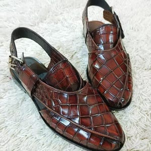 Luxury brown crocodile-textured leather slingback sandals for men with pointed toe and buckle strap detail, handmade premium formal footwear styled with beige trousers in an elegant indoor setting.