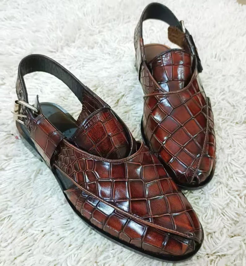 Luxury brown crocodile-textured leather slingback sandals for men with pointed toe and buckle strap detail, handmade premium formal footwear styled with beige trousers in an elegant indoor setting.