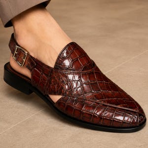 Luxury brown crocodile-textured leather slingback sandals for men with pointed toe and buckle strap detail, handmade premium formal footwear styled with beige trousers in an elegant indoor setting.