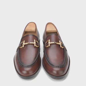 Handmade mahogany brown leather horsebit loafers for men featuring a gold metal horsebit, moc toe stitching, premium leather construction, and classic slip-on design for formal and business casual wear.