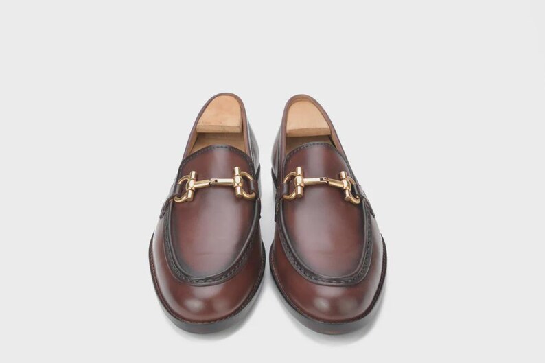 Handmade mahogany brown leather horsebit loafers for men featuring a gold metal horsebit, moc toe stitching, premium leather construction, and classic slip-on design for formal and business casual wear.