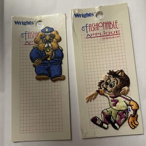 Peut inclure: Deux écussons vintage Wrights Fashionable Applique. L'un représente un ours en uniforme de policier, l'autre un singe en uniforme de baseball. Les deux sont sur un support quadrillé avec le nom de la marque et la description du produit.