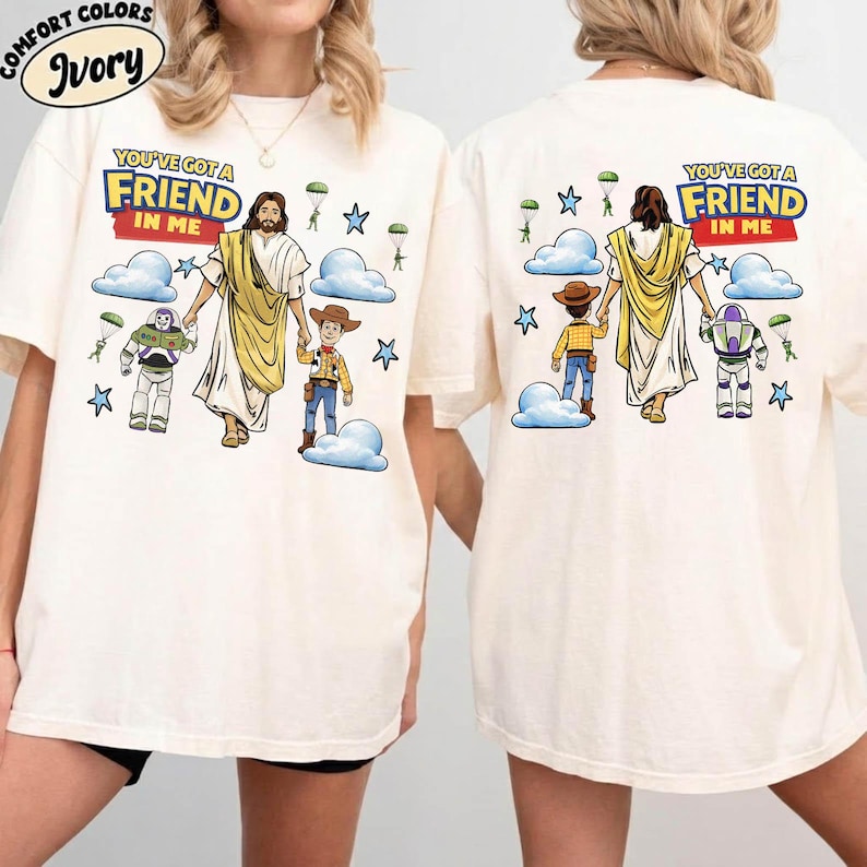 May include: Ivory-coloured t-shirts featuring the text "YOU'VE GOT A FRIEND IN ME" and a graphic of Jesus with cartoon characters. The design includes clouds, stars, and parachutes. The shirts are a Comfort Colors brand.