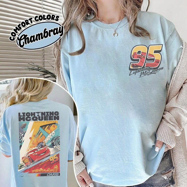 May include: Light blue t-shirt with "95 Lightning McQueen" graphic on the front and a larger graphic on the back. The back graphic features Lightning McQueen racing, with the text "Lightning McQueen" and "Cars". The shirt is labeled "Comfort Colors Chambray".