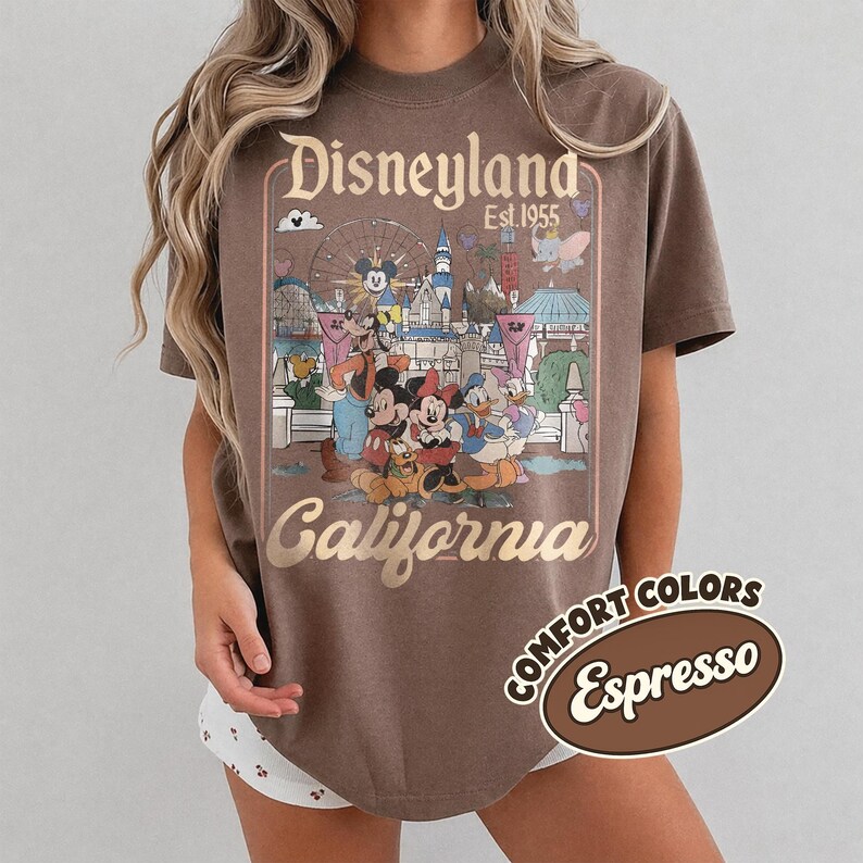 Może przedstawiać: Koszulka w kolorze espresso z grafiką Disneyland California. Projekt zawiera logo Disneyland, rok 1955 oraz postacie z kresk&oacute;wek, takie jak Myszka Miki i Kaczor Donald. Koszulka jest oznaczona jako "Comfort Colors".