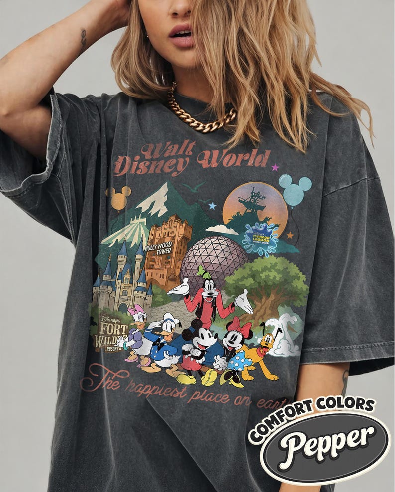 Pu&ograve; includere: T-shirt grigio scuro con una grafica colorata dei monumenti e dei personaggi di Disney World. Il design include il testo "Walt Disney World", "Hollywood Tower" e "The happiest place on earth". La maglietta ha un aspetto vintage.