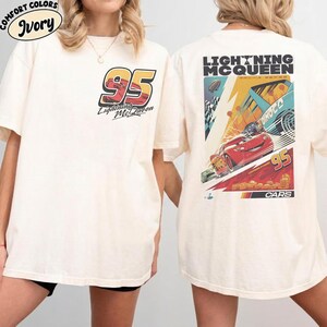 May include: Ivory-colored t-shirt featuring the number 95 and the words "Lightning McQueen" in a racing-themed design on the front. The back of the shirt displays a colorful graphic with Lightning McQueen and the text "Lightning McQueen Racing Series".