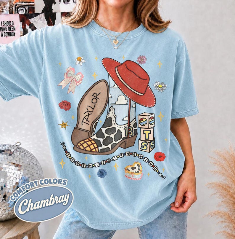 Peut inclure: Un t-shirt bleu clair avec une impression graphique repr&eacute;sentant un chapeau de cowboy rouge, une botte de cowboy &agrave; motif vache avec le nom Taylor et le chiffre 13, des blocs empil&eacute;s avec les lettres T, S et un collier de perles avec le texte I KNEW IT WHEN YOU.
