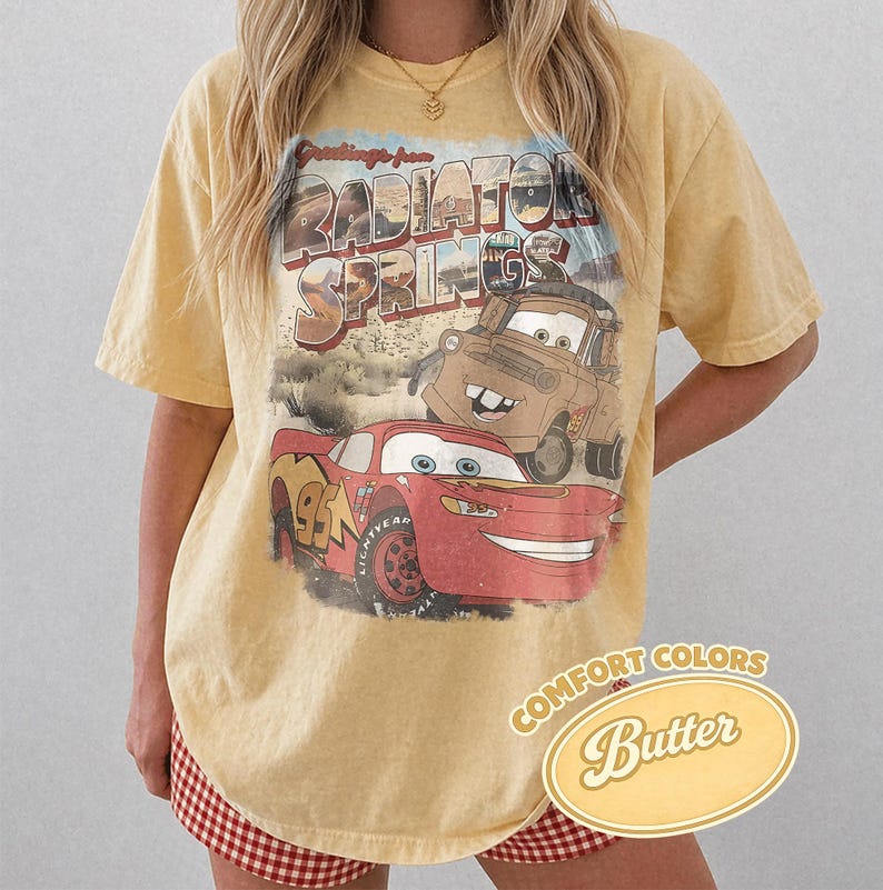 May include: A yellow t-shirt featuring a graphic of Lightning McQueen and Mater from the movie Cars, with the words "Radiator Springs" above them. The shirt has a vintage look and the words "Comfort Colors Butter" are printed on the bottom right.