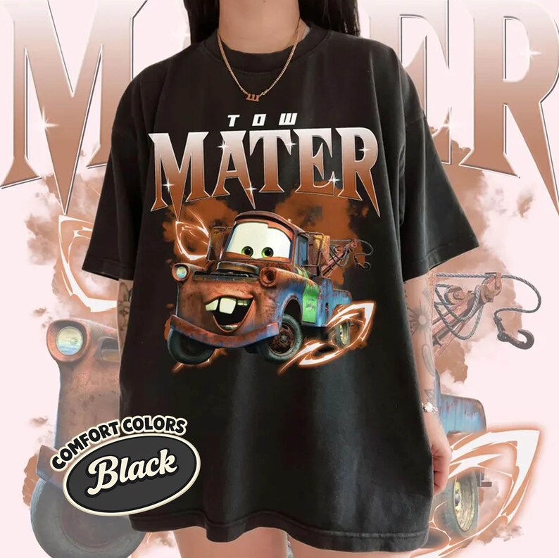 May include: Black t-shirt featuring the character Mater from the movie Cars. The design includes the text "TOW MATER" in a bold font above an image of Mater. The shirt also has the words "COMFORT COLORS" and "Black" in a circular design.