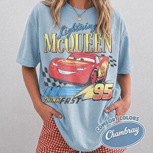 K&ouml;nnte beinhalten: Hellblaues T-Shirt mit einem Lightning McQueen-Motiv aus dem Film Cars. Die Grafik zeigt den Schriftzug "Lightning McQueen", die Nummer "95" und den Satz "Think Fast". Das T-Shirt hat einen Vintage-Look.