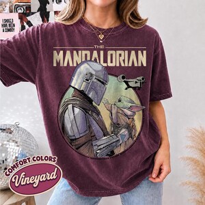 Puede incluir: Una camiseta de manga corta color granate oscuro con un gr&aacute;fico circular de The Mandalorian y Grogu. El texto THE MANDALORIAN est&aacute; impreso sobre el gr&aacute;fico, que tambi&eacute;n muestra una peque&ntilde;a nave espacial. La camiseta tiene un aspecto vintage.