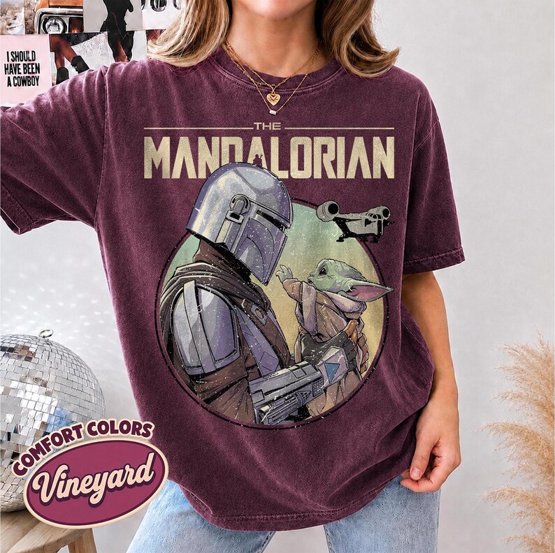 Puede incluir: Una camiseta de manga corta color granate oscuro con un gr&aacute;fico circular de The Mandalorian y Grogu. El texto THE MANDALORIAN est&aacute; impreso sobre el gr&aacute;fico, que tambi&eacute;n muestra una peque&ntilde;a nave espacial. La camiseta tiene un aspecto vintage.