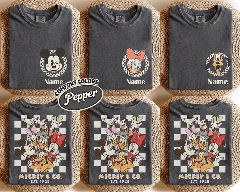 May include: Dark gray t-shirts featuring Disney characters Mickey Mouse, Daisy Duck, and Pluto. The shirts have a round neck and short sleeves. Some shirts have a character's face in a checkered circle, with the word "Name" below. Other shirts have a group of characters with the text "MICKEY & CO. EST. 1928".