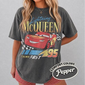 K&ouml;nnte beinhalten: Dunkelgraues T-Shirt mit Lightning McQueen aus dem Film Cars. Das Design zeigt die Figur, die Nummer 95 und die Worte "Lightning McQueen" und "Think Fast". Das Shirt hat auch den Text "Comfort Colors" und "Pepper".