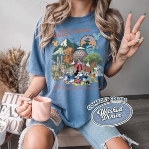 Pu&ograve; includere: T-shirt blu Comfort Colors con una grafica colorata di personaggi e monumenti di Disney World. La maglietta include il testo "Walt Disney World" e "The happiest place on earth". La maglietta &egrave; etichettata come "Washed Denim".