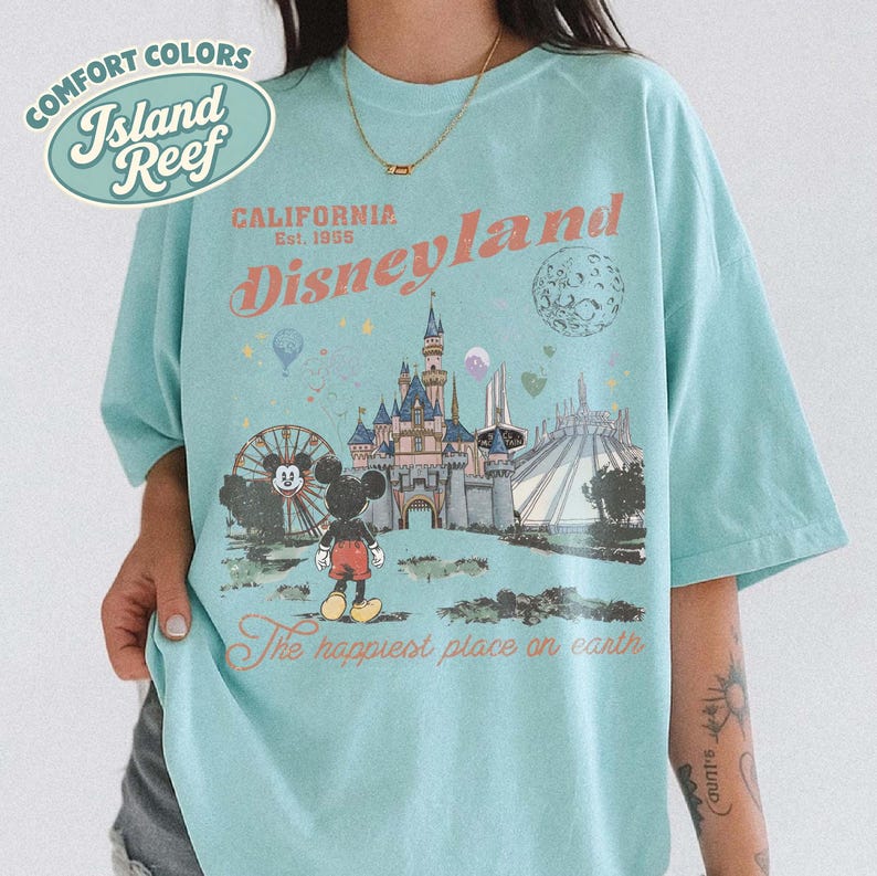 May include: A light blue t-shirt with a Disneyland graphic. The graphic features a castle, Mickey Mouse, and the words "Disneyland" and "The happiest place on earth." The shirt also has the words "Comfort Colors" and "Island Reef."