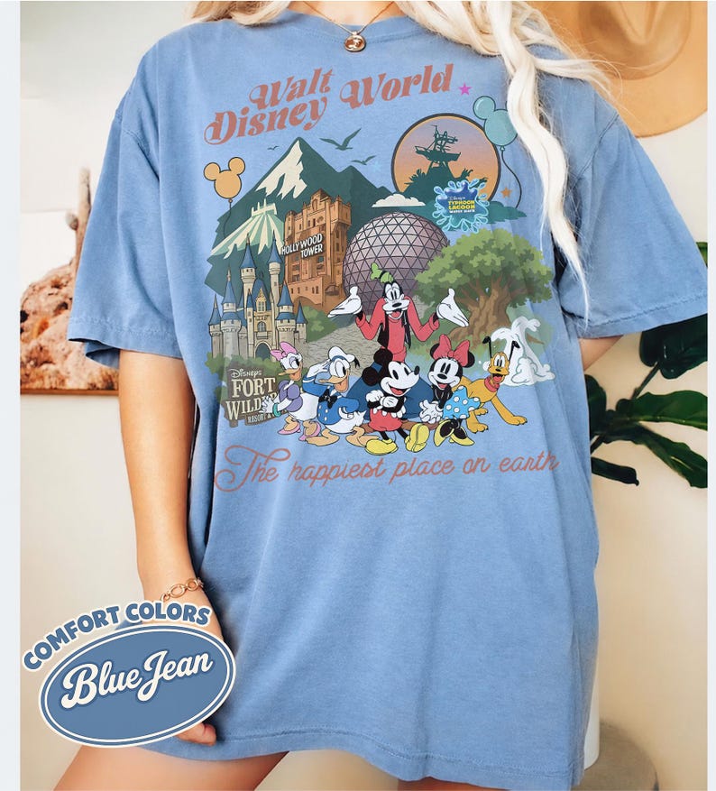 Pu&ograve; includere: T-shirt Comfort Colors blu jeans con grafica colorata di personaggi e monumenti di Disney World. La maglietta include il testo "Walt Disney World" e "The happiest place on earth."