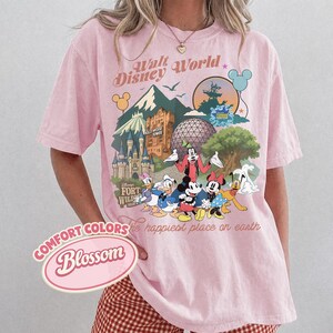 Pu&ograve; includere: T-shirt rosa chiaro con una grafica di personaggi e monumenti Disney, tra cui un castello, la Hollywood Tower e Spaceship Earth. Sono visibili anche le scritte "Walt Disney World" e "the happiest place on earth". La maglietta ha il testo "Comfort Colors Blossom".