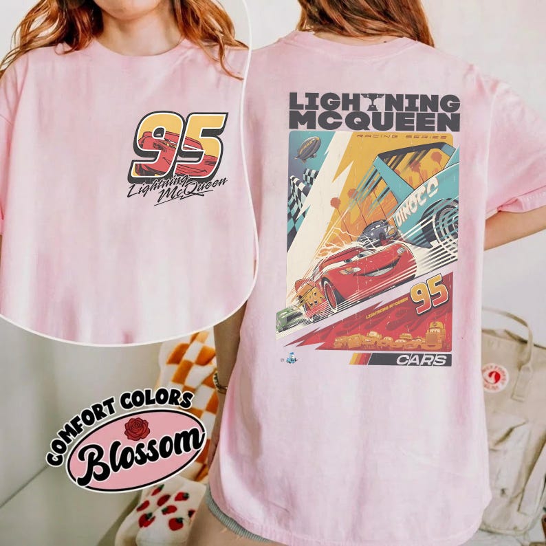 May include: A light pink t-shirt featuring the number "95" and "Lightning McQueen" on the front. The back of the shirt displays a colorful graphic of Lightning McQueen racing, with the text "Lightning McQueen" and "Cars".